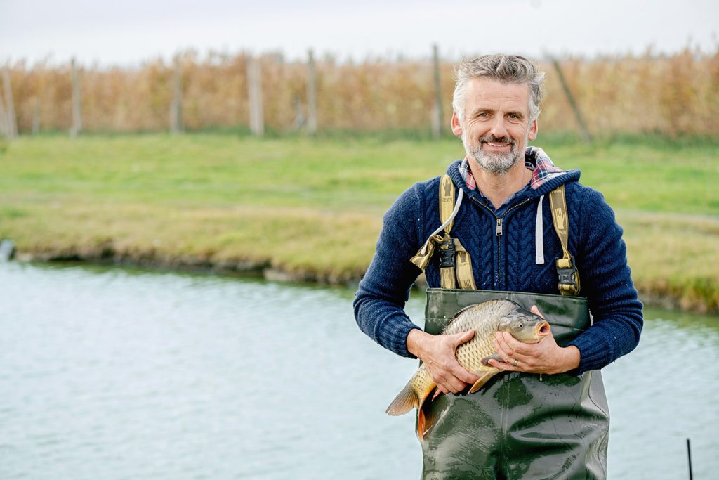Fischer Robert Jungwirth am Teich mit Karpfen in der Hand.
