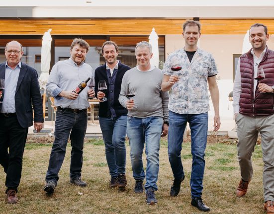 Die vier Winzer und Weintourismus-Obmann Herbert Oschep sowie Weinbaupräsident Andreas Liegegeld mit einem Glas Rotwein in der Han auf einer Wiese.
