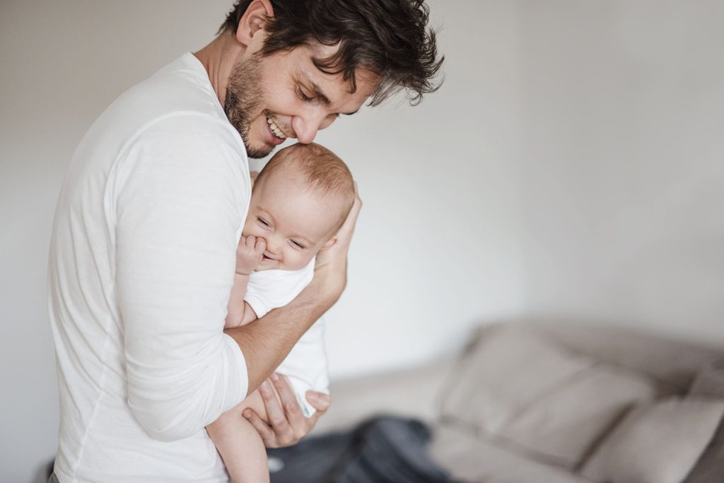 Lächelnder Vater hält lachendes Baby im Arm.
