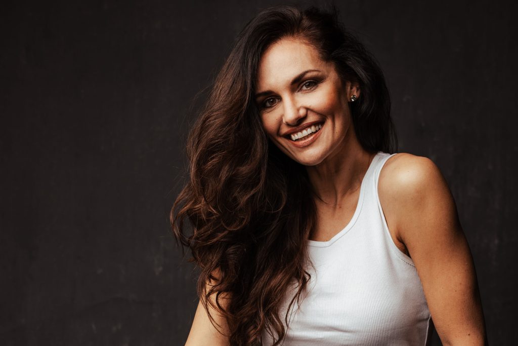 Model Tanja Duhovich in einem weißen Tank-Top vor einem dunklen Hintergrund.