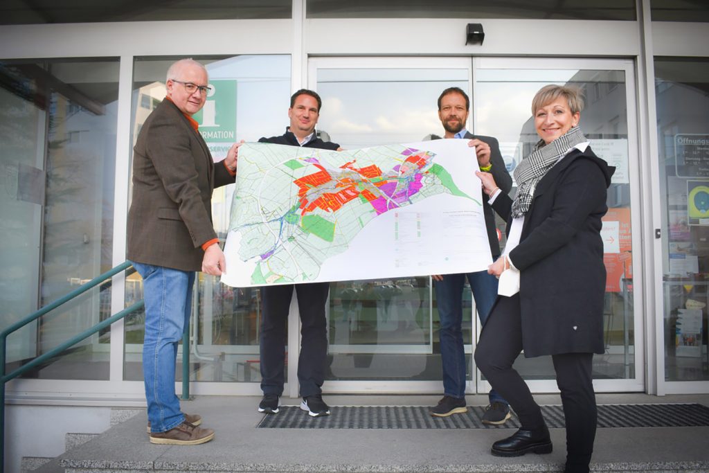 Bürgermeisterin von Mattersburg Claudia Schlager mit ihrem Team halten eine Karte mit farbigen Zonen von Mattersburg in der Hand.