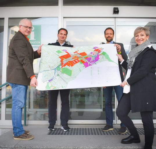Bürgermeisterin von Mattersburg Claudia Schlager mit ihrem Team halten eine Karte mit farbigen Zonen von Mattersburg in der Hand.