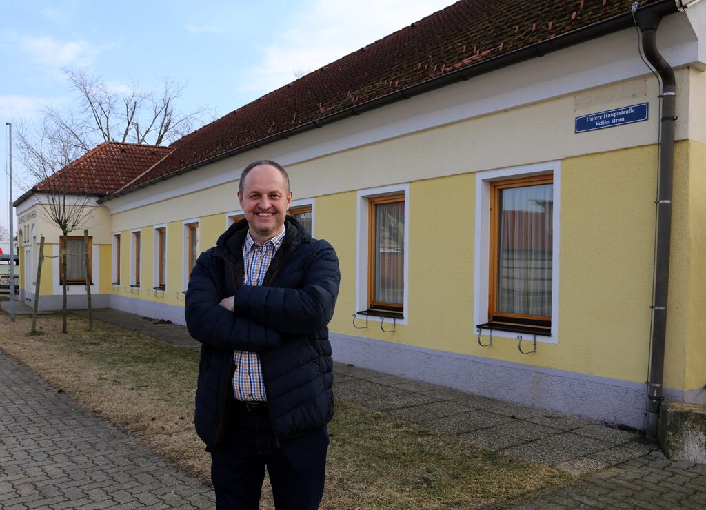 Bürgermeister von Neudorf Karel Lentsch vor einem gelben Gebäude in der Gemeinde.