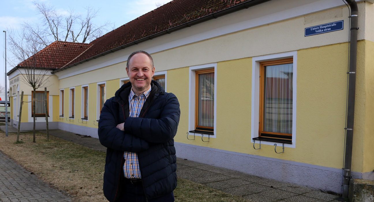 Bürgermeister von Neudorf Karel Lentsch vor einem gelben Gebäude in der Gemeinde.