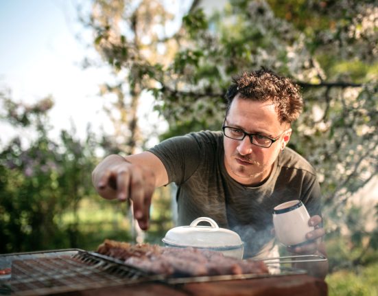 Mann salzt sein Steak am Griller
