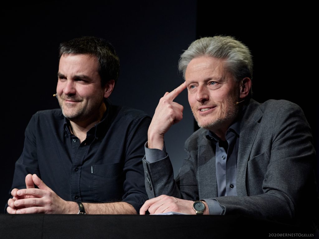 Florian Klenk und Florian Scheuba sitzen nebeneinander vor einem schwarzen Hintergrund.