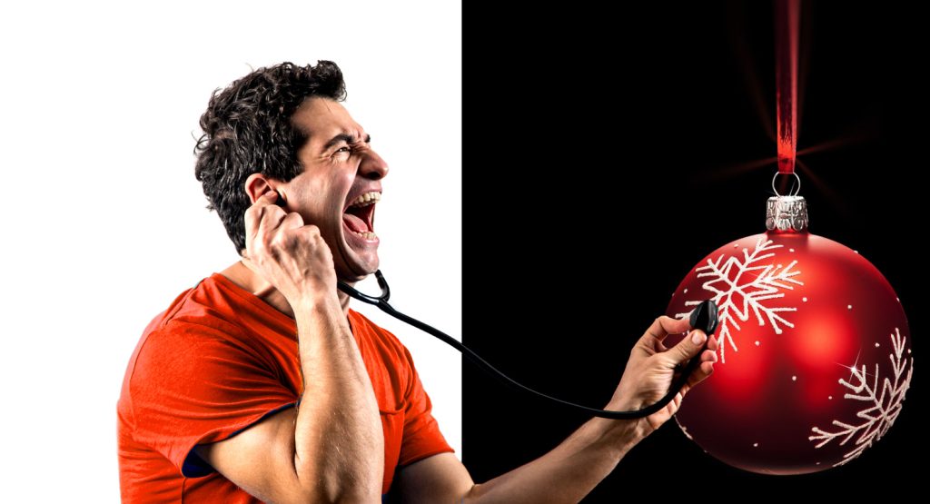 Kabarettist Omar Sarsam mit einem rotem T-Shirt auf weißem und schwarzem Hintergrund, während er mit einem Stethoskop eine Christbaumkugel abhört.