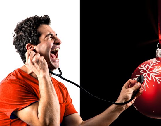 Kabarettist Omar Sarsam mit einem rotem T-Shirt auf weißem und schwarzem Hintergrund, während er mit einem Stethoskop eine Christbaumkugel abhört.
