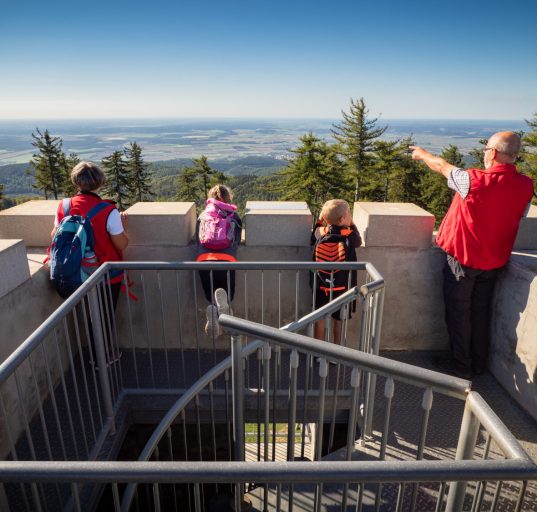 Man und drei Kinder stehen auf dem Aussichtsturm Geschriebenstein und genießen den Ausblick.