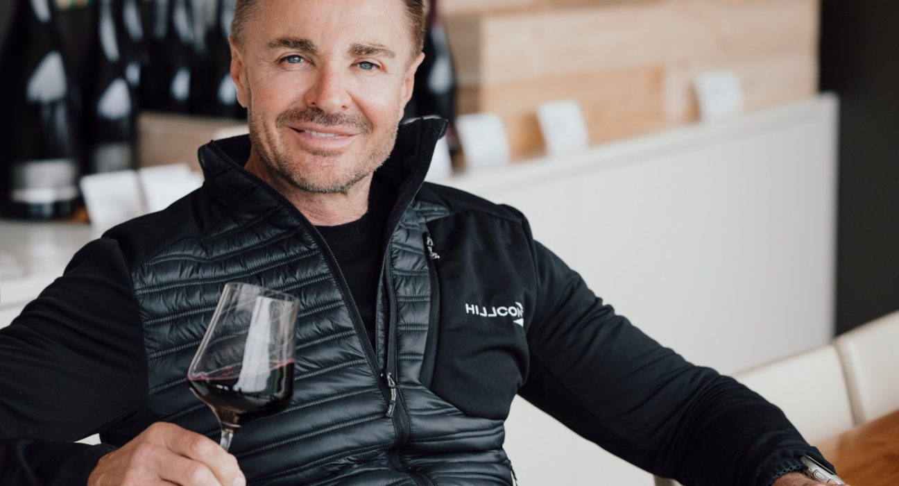 Leo Hillinger sitzt bei einem Tisch mit einem Glas Wein in der Hand