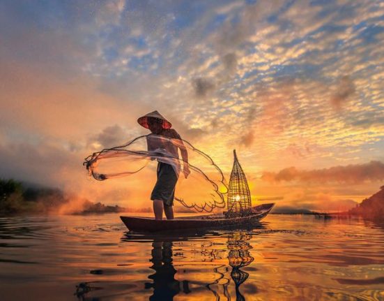 Fischer steht in einem kleinen Boot in der Abenddaämmerung am Mekong