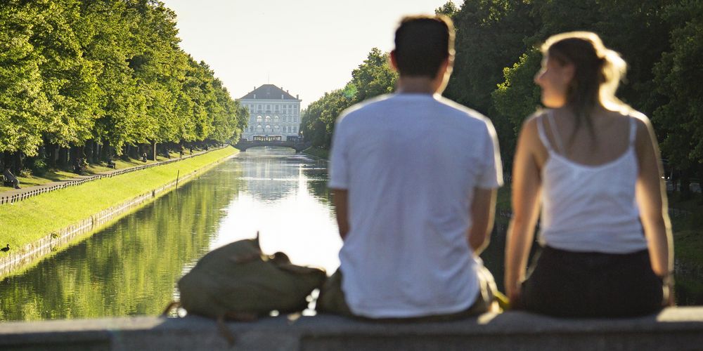 Ein Paar sitzt auf einer Brücke mit Blick auf das Schloss Nymphenburg