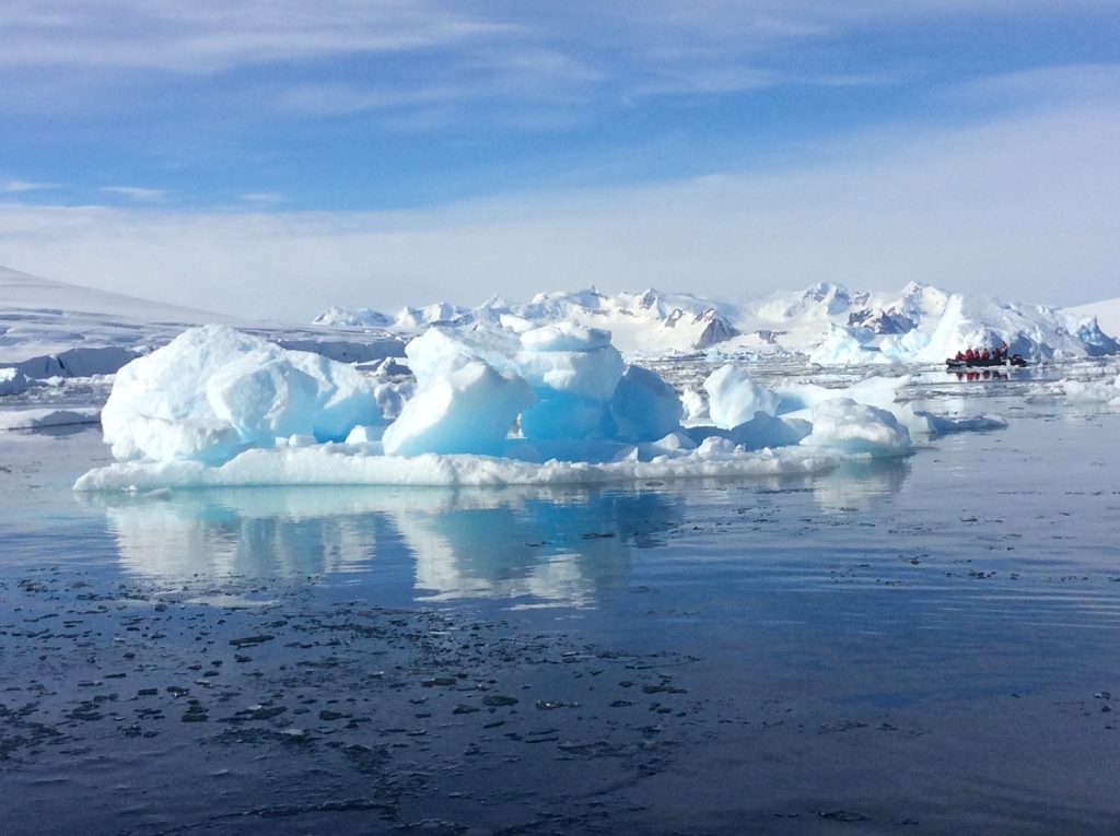 Eisschollen treiben im antarktischen Meer, im Hintergrund ein Schlauchboot mit Expeditionsteilnehmern