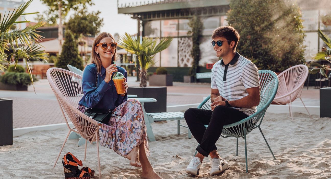 Junge Frau und junger Mann sitzen entspannt am Beach im Designer Outlet Parndorf