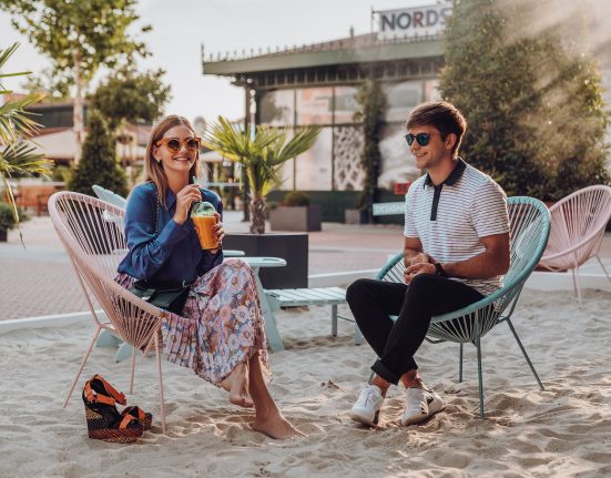 Junge Frau und junger Mann sitzen entspannt am Beach im Designer Outlet Parndorf