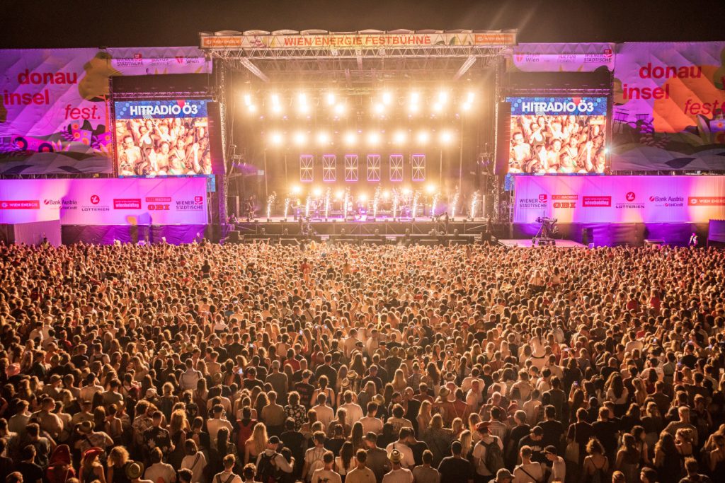 Die Bühne am Donauinselfest hell erleuchtet mit Menschenmassen davor.