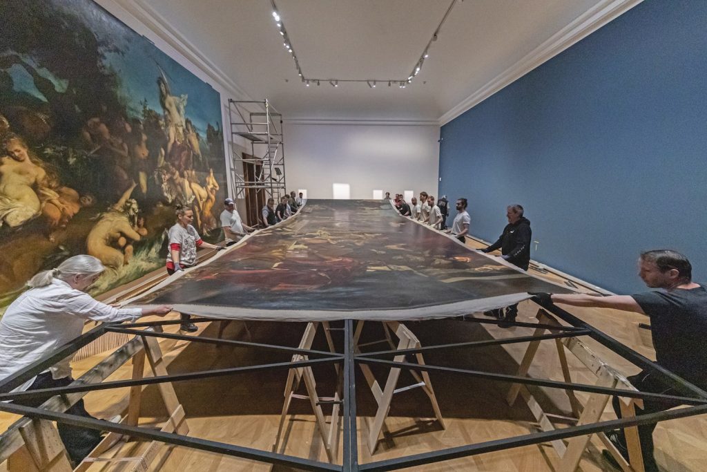 16 Menschen spannen ein riesiges Gemälde über einen Rahmen. Es wird später einen ganze kolossale Wand einnehmen. © Johannes Stoll / Belvedere, Wien