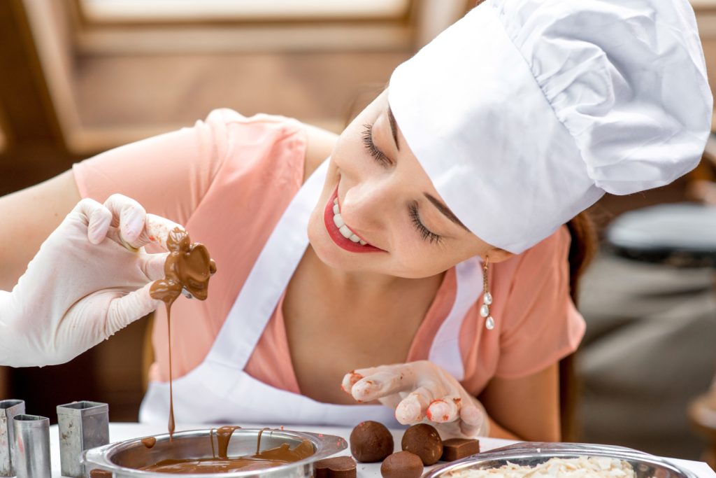 Frau macht handgemachte Pralinen und tunkt Praline in Schokolade
