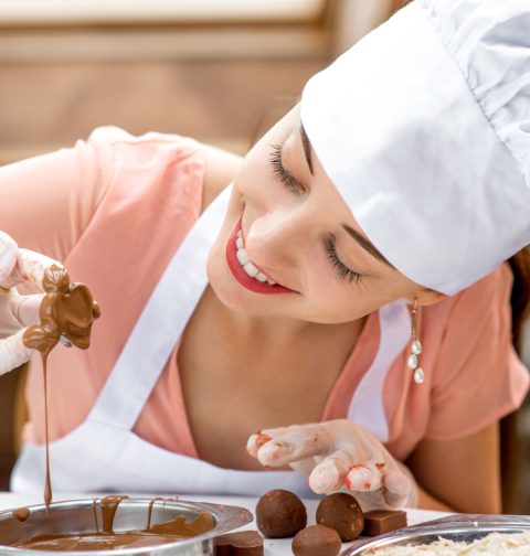 Frau macht handgemachte Pralinen und tunkt Praline in Schokolade