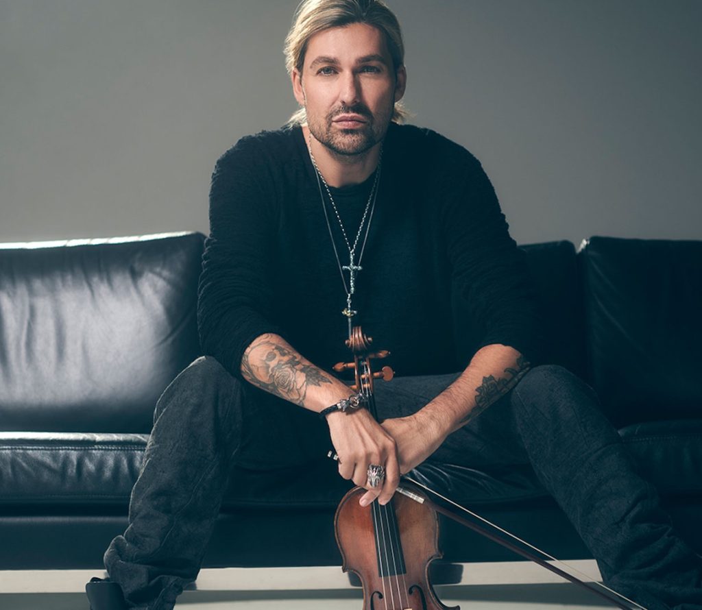 David Garrett sitzt auf einem Sofa und hält seine Geige lässig in der Hand. © Christoph Koestlin