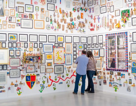 Eine Ecke in der Ausstellung „gugging.! classic & contemporary“: ein Mann und eine Frau vor vielen Bildern und Objekten @ NÖ Museum Betriebs GmbH, Ludwig Schedl