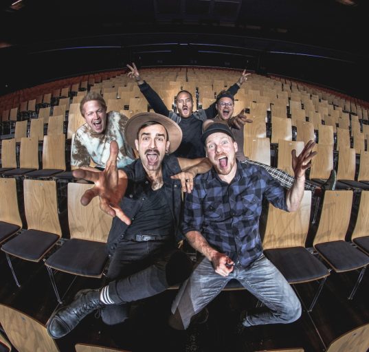 Mitglieder der Fäaschtbänkler in einem leeren Saal lachen in die Kamera