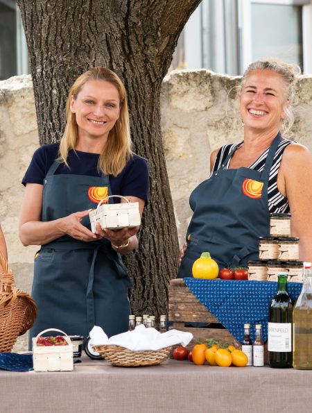 drei Frauen vor einem Tisch mit kulinarischen Spezialitäten lächeln in die Kamera