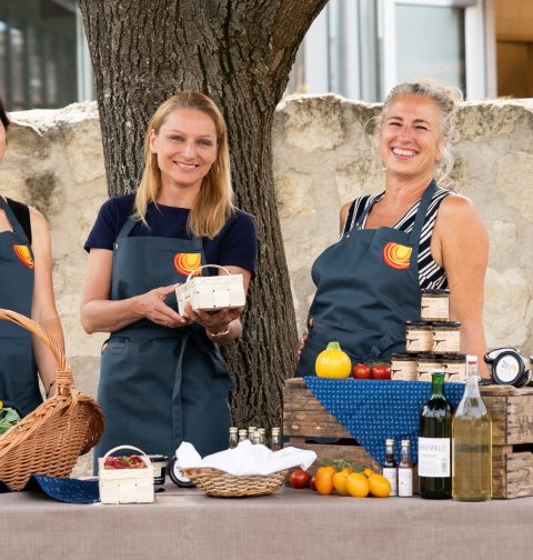 drei Frauen vor einem Tisch mit kulinarischen Spezialitäten lächeln in die Kamera