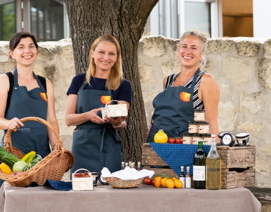 drei Frauen vor einem Tisch mit kulinarischen Spezialitäten lächeln in die Kamera