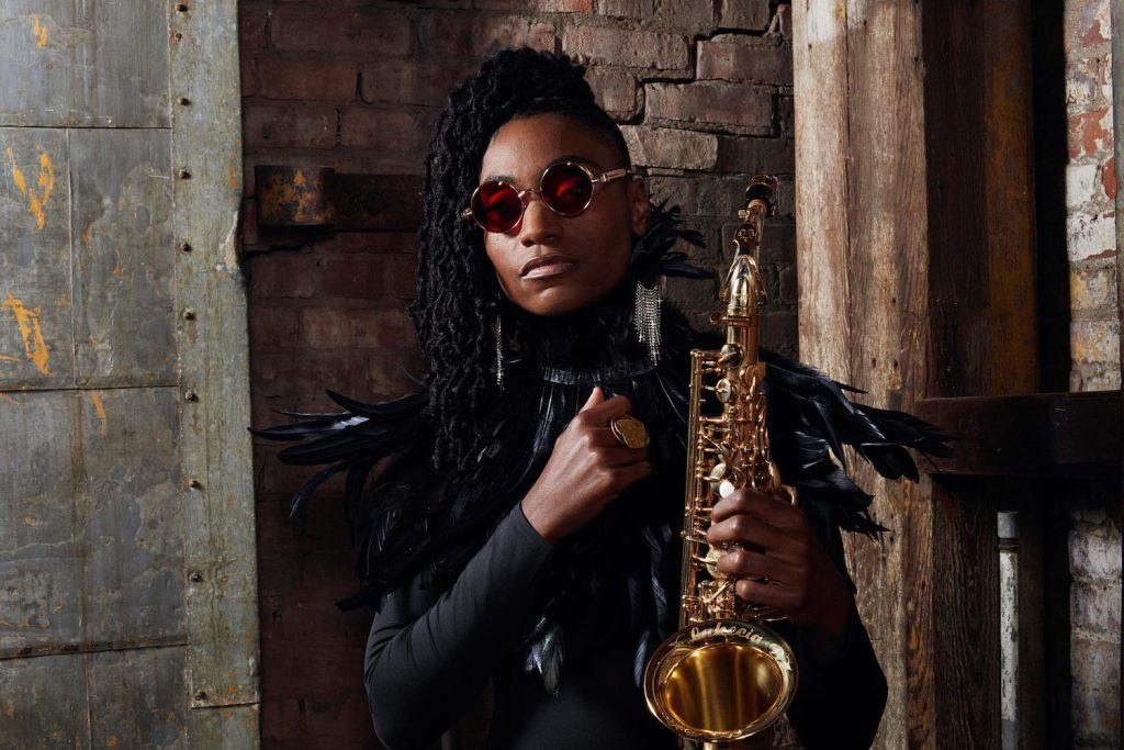 Eine schwarze Musikerin (Lakecia Benjamin) mit ihrem Saxophon vor einer Ziegelwand © Benjamin/Porgy