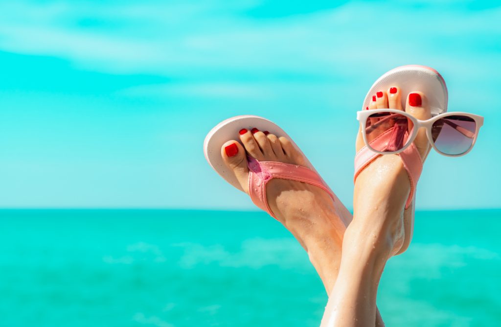 Füße mit Sonnenbrille vor türkisblauem Meer