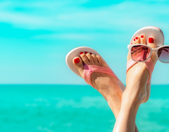 Füße mit Sonnenbrille vor türkisblauem Meer