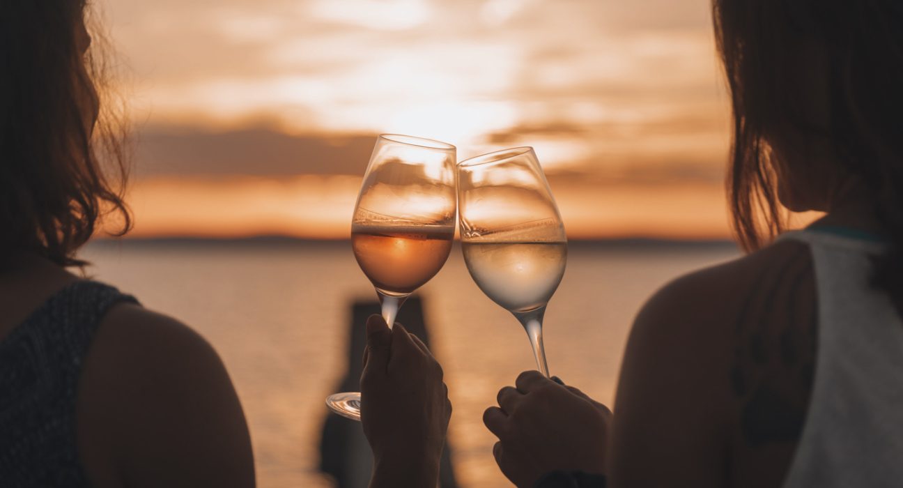 Sicht auf den See und zwei Damen stoßen mit Weingläsern an