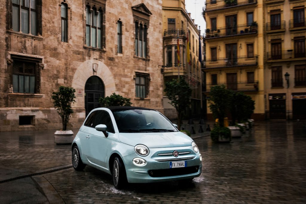 Der Kleinwagen Fiat 500 in blitzblau geparkt auf nassem Kopfsteinpflaster vor italienischen Bauten.