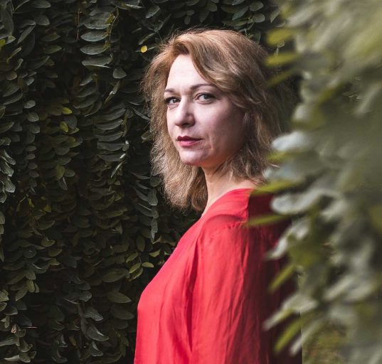 Anastasia Voltchok in roter Bluse, umgeben von Büschen © Anastasia Voltchok