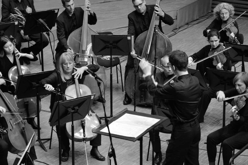 Die Geigerinnen und Geiger eines kleinen Orchesters mit einem jungen Dirigenten im Vordergrund. © Sonja Stangl