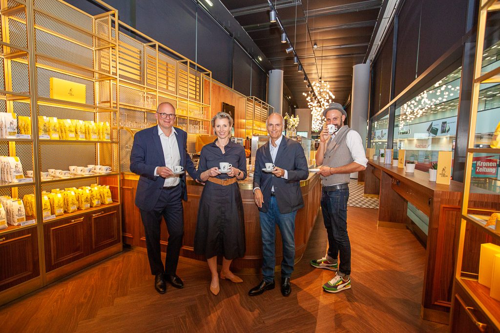 Von Links: Vorstand der Flughafen Wien AG Julian Jäger, CEO Lagardère Travel Retail Austria Ursula Fürnhammer sowie Rudi Kobza und Valentin Siglreithmaier, Mitarbeiter von Bieder & Maier mit Kaffeetassen in der Hand im Café.