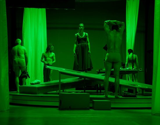 Eine dunkle Bühne, in grünes Licht getaucht. Vorhänge im Vorder- und Hintergrund. Fünf Menschen stehen da, die Männer mit nacktem Oberkörper. („Dunkelblum“) © Franzi Kreis