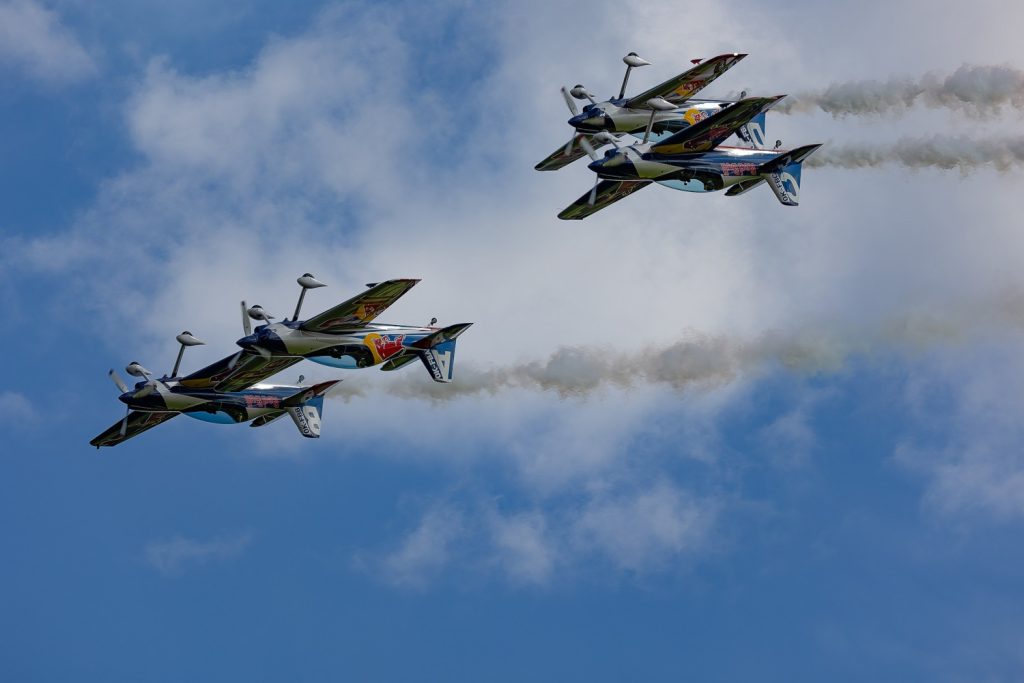 vier Red-Bull Flugzeuge im Himmel während einer Airshow, links fliegen zwei dicht nebeneinander, rechts zwei übereinander