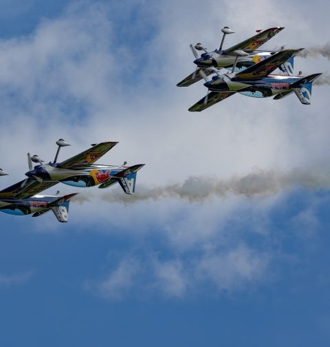 vier Red-Bull Flugzeuge im Himmel während einer Airshow, links fliegen zwei dicht nebeneinander, rechts zwei übereinander