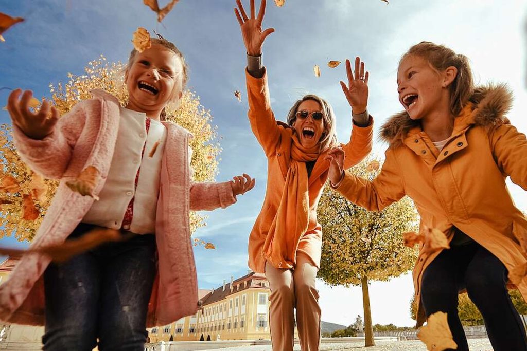 Eine Frau und zwei Mädchen freuen sich vor Schloss Hof, dass das Herbstlaub fällt. © Schloss_Schoenbrunn_Kultur-_und_BetriebsgesmbH_Michal_Cilc