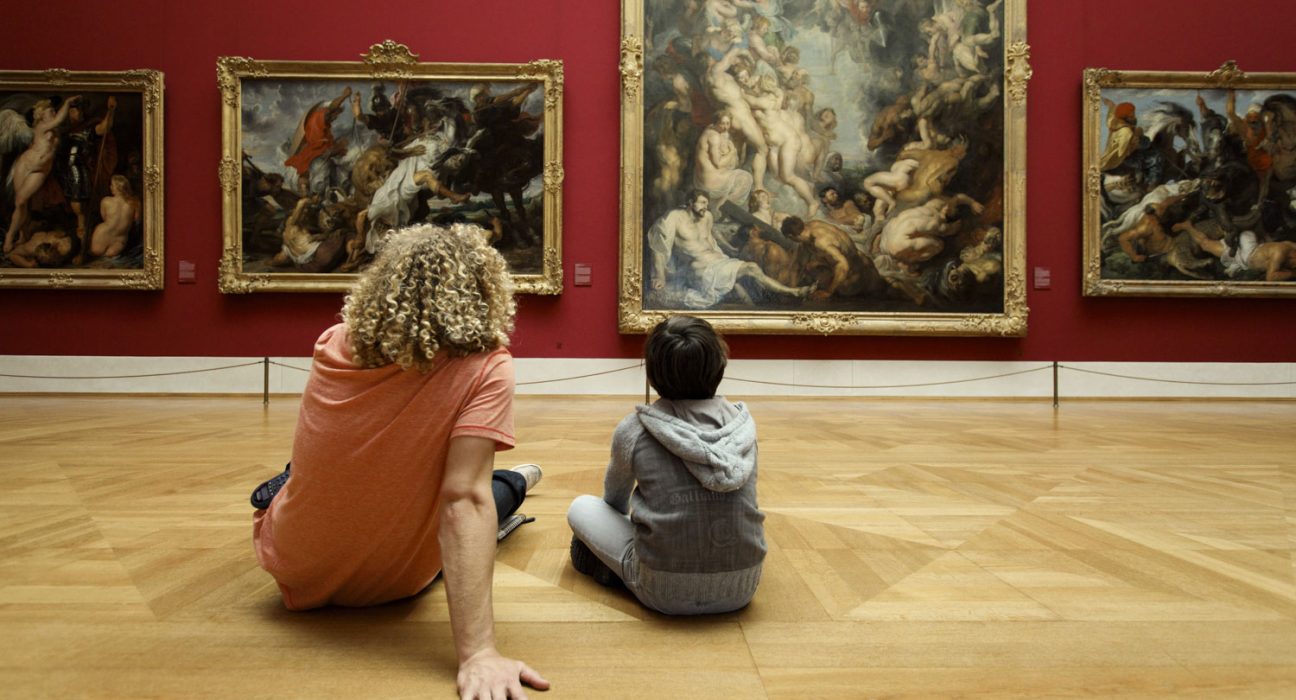 Zwei Besucher sitzen am Boden vor Kunstwerken in der Alten Pinakothek von München