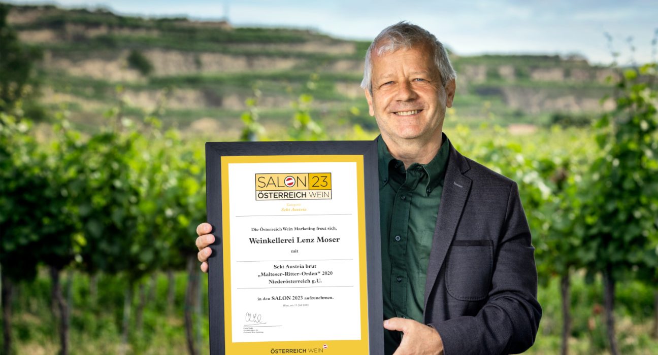 Chef Önologe von Lenz Moser mit der Urkunde in der Hand vor einem Weingarten.