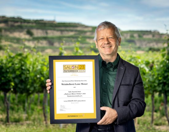 Chef Önologe von Lenz Moser mit der Urkunde in der Hand vor einem Weingarten.