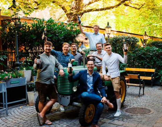 Die glücklichen Nominierten der Schlossquadart Trophy auf einem grünen Traktor sitzend in einem Innenhof auf Pflastersteinen.