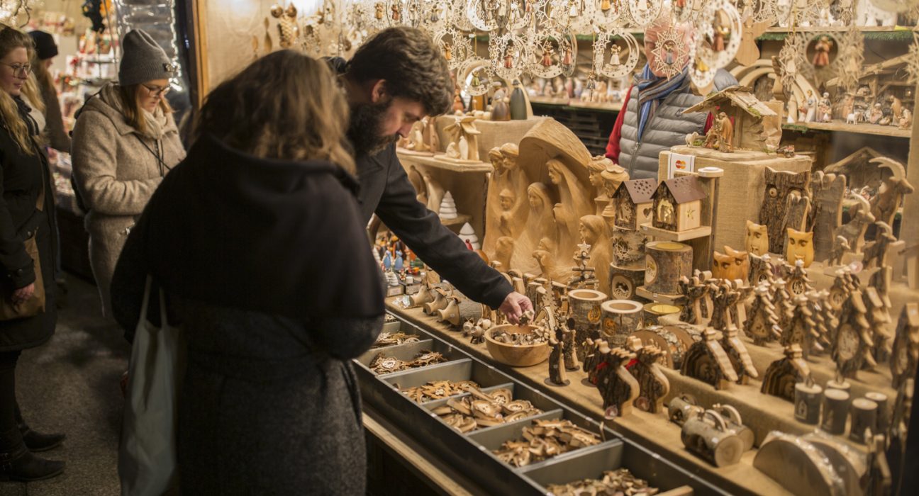 Mann und Frau begutachten Holzschnitzerein am Weihnachtsmarkt.