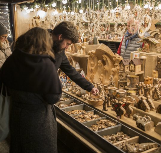 Mann und Frau begutachten Holzschnitzerein am Weihnachtsmarkt.