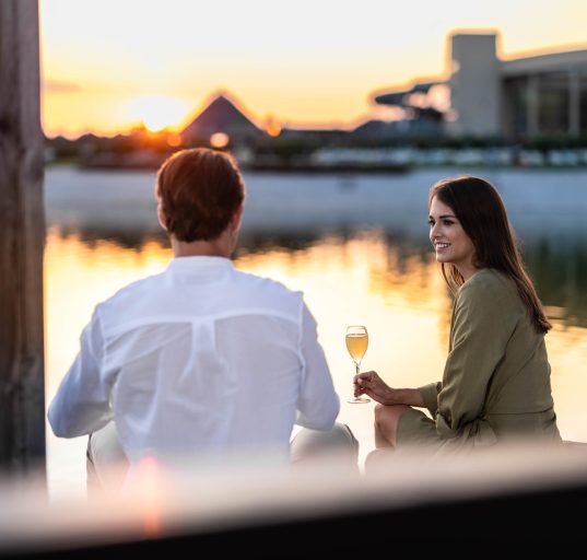 Pärchen sitzt mit einem Weinglas in der Hand vor der malerischen Kulisse der St. Martins Therme bei Sonnenuntergang beim Wein- und Genussfest.