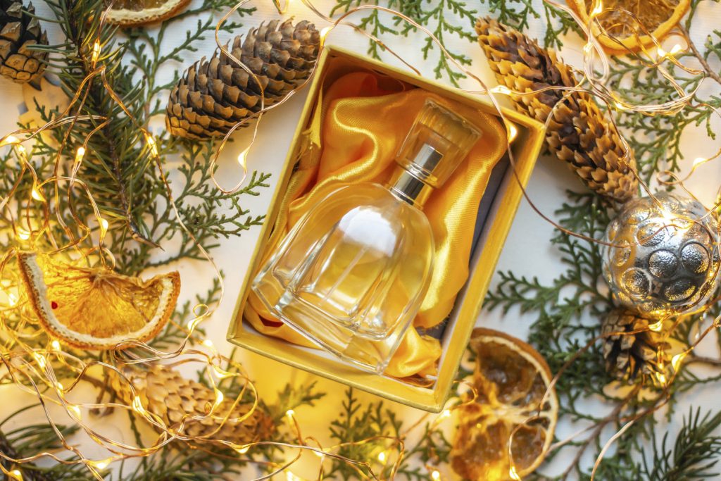 Parfumflasche in Box auf orangem Tuch, ringsum Dekoration aus Tannenzapfen, Blättern, getrockneten Orangen und Lichterkette