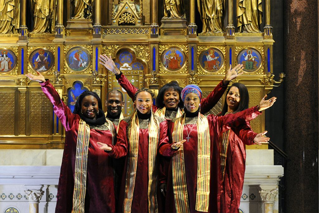 Stella Jones unjd ihr Christmas Gospel Chor in roten Roben vor goldenem Altar.